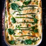 overhead view of baked lasagna in pan garnished with asparagus and spinach